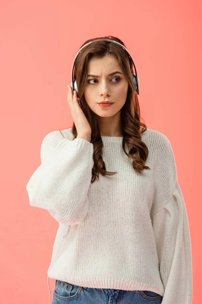Mujer seria y atractiva en suéter blanco con auriculares aislados en rosa - foto de stock
