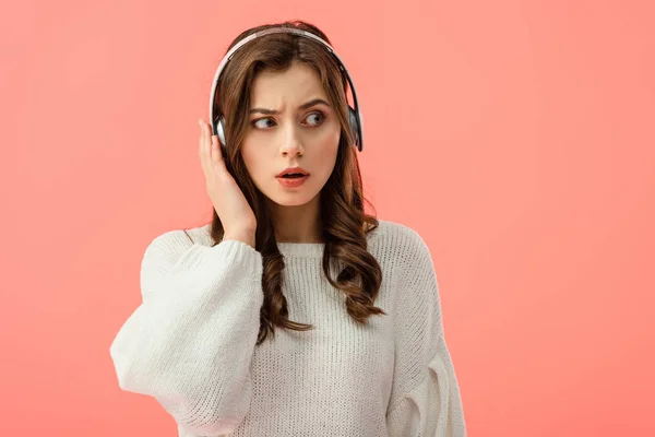 Schockierte und attraktive Frau in weißem Pullover mit Kopfhörern auf rosa — Stockfoto