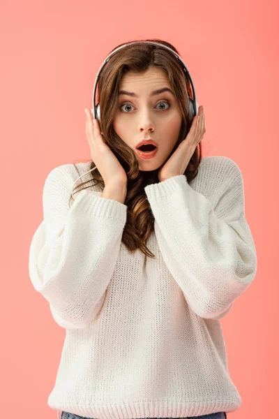 Shocked and beautiful woman in white sweater with headphones isolated on pink — Stock Photo