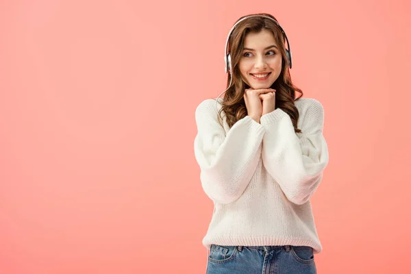 Smiling and happy woman in white sweater listening music with headphones isolated on pink — Stock Photo