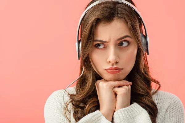 Sad woman in white sweater listening music with headphones isolated on pink — Stock Photo