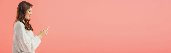 Plan panoramique de femme souriante et séduisante en pull blanc tenant smartphone isolé sur rose — Photo de stock