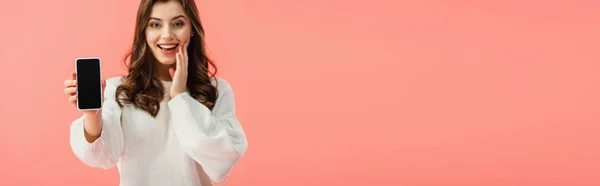 Colpo panoramico di donna sorridente e bella in maglione bianco che tiene smartphone con spazio copia isolato su rosa — Foto stock