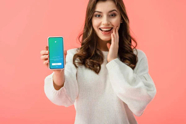 Selektiver Fokus einer Frau im weißen Pullover, die ihr Smartphone mit Twitter-App auf dem Bildschirm isoliert auf rosa hält — Stockfoto