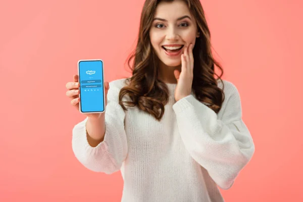 Selektiver Fokus einer Frau im weißen Pullover, die ihr Smartphone mit Skype-App auf dem Bildschirm isoliert auf rosa hält — Stockfoto