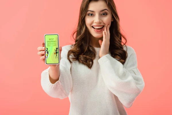 Foyer sélectif de la femme en pull blanc tenant smartphone avec la meilleure application shopping à l'écran isolé sur rose — Photo de stock