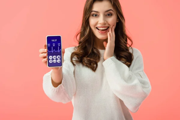 Selective focus of woman in white sweater holding smartphone with health app on screen isolated on pink — Stock Photo