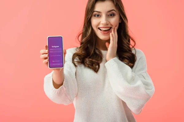 Selective focus of woman in white sweater holding smartphone with instagram app on screen isolated on pink — Stock Photo