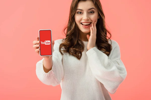 Foyer sélectif de la femme en pull blanc tenant smartphone avec application youtube à l'écran isolé sur rose — Photo de stock