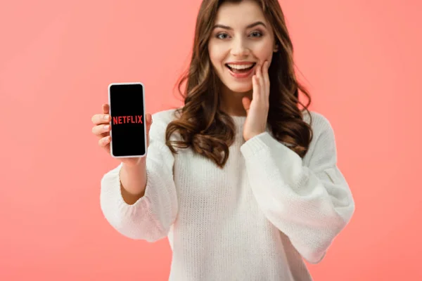 Selektiver Fokus der Frau im weißen Pullover, Smartphone mit Netflix-App auf dem Bildschirm isoliert auf rosa — Stockfoto