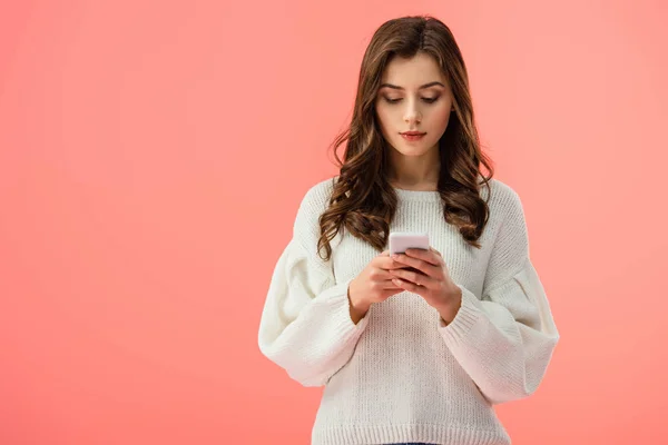 Hermosa mujer joven en suéter blanco sosteniendo teléfono inteligente aislado en rosa - foto de stock