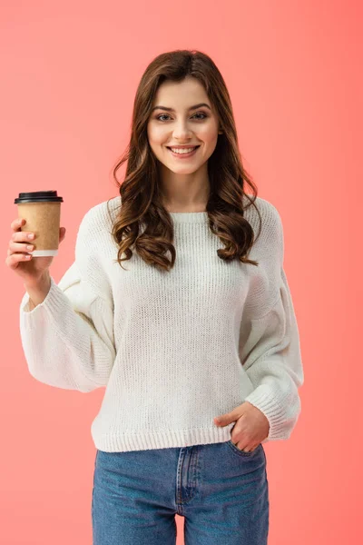 Mujer joven sonriente y atractiva en suéter blanco sosteniendo una taza de papel aislada en rosa — Stock Photo