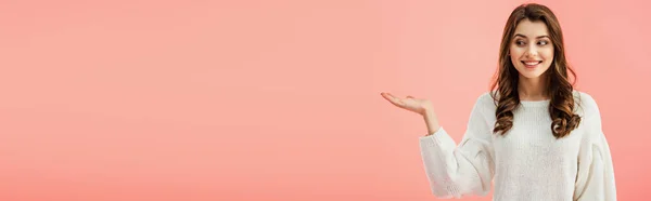 Panoramic shot of beautiful woman in white sweater pointing with hand isolated on pink — Stock Photo