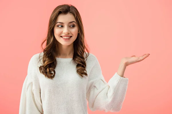 Smiling and beautiful woman in white sweater pointing with hand isolated on pink — Stock Photo