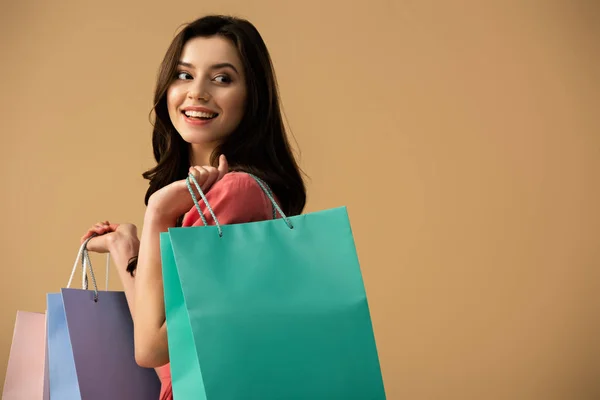 Smiling and beautiful woman holding shopping bags isolated on beige — Stock Photo