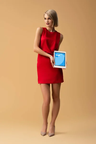 Вид женщины в красном платье в полный рост, держащей цифровой планшет с приложением на экране — стоковое фото