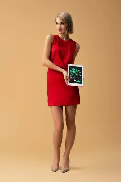 Вид женщины в красном платье в полный рост, держащей цифровую таблицу с графиками и графиками на экране — стоковое фото