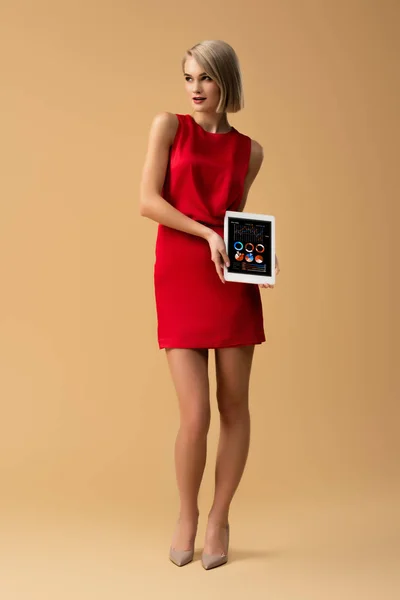 Visão de comprimento total da mulher em vestido vermelho segurando tablet digital com gráficos e gráficos na tela — Fotografia de Stock