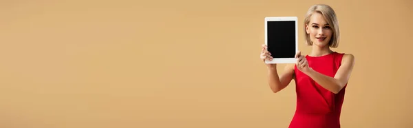 Panoramaaufnahme einer Frau im roten Kleid, die ein digitales Tablet mit leerem Bildschirm hält, isoliert auf beige — Stockfoto
