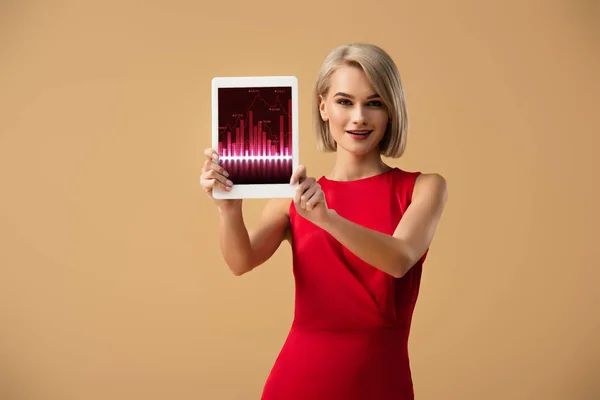 Hermosa mujer en vestido rojo sosteniendo tableta digital con aplicación de comercio en la pantalla aislada en beige - foto de stock