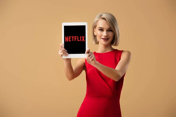 Красивая женщина в красном платье держит цифровой планшет с netflix приложение на экране изолированы на бежевый — стоковое фото