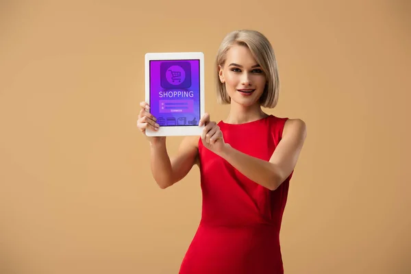 Schöne Frau im roten Kleid hält digitales Tablet mit Shopping-App auf dem Bildschirm isoliert auf beige — Stockfoto