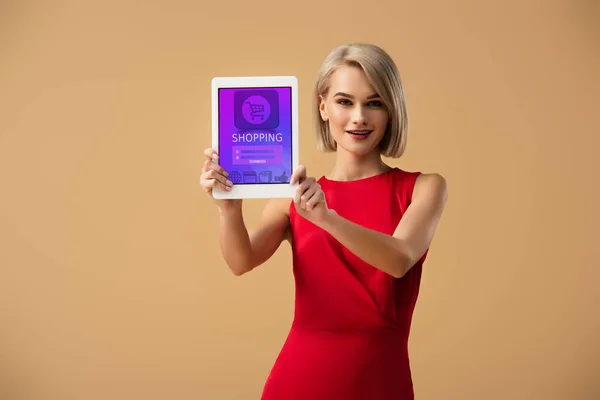 Belle femme en robe rouge tenant tablette numérique avec app shopping à l'écran isolé sur beige — Photo de stock