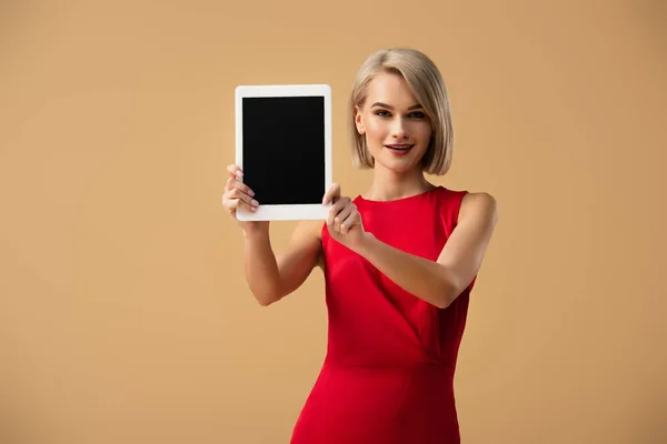 Hermosa mujer en vestido rojo sosteniendo tableta digital con pantalla en blanco aislado en beige - foto de stock