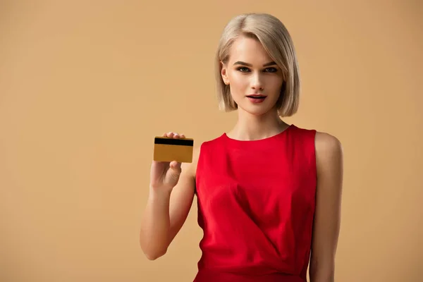 Hermosa joven en vestido rojo con tarjeta de crédito aislada en beige - foto de stock