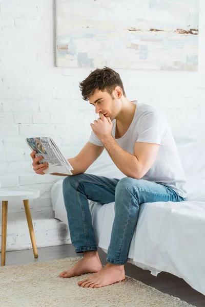 Schöner Mann sitzt zu Hause auf dem Bett und liest Zeitung — Stockfoto