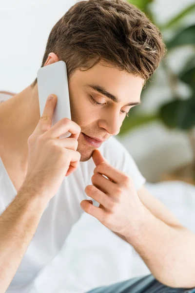 Selective focus of handsome man in white t-shirt talking on smartphone at home — Stock Photo