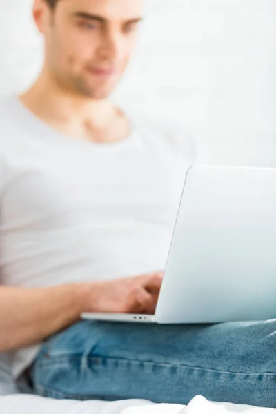 Enfoque selectivo del hombre en camiseta sentado y escribiendo en el ordenador portátil sobre fondo blanco - foto de stock