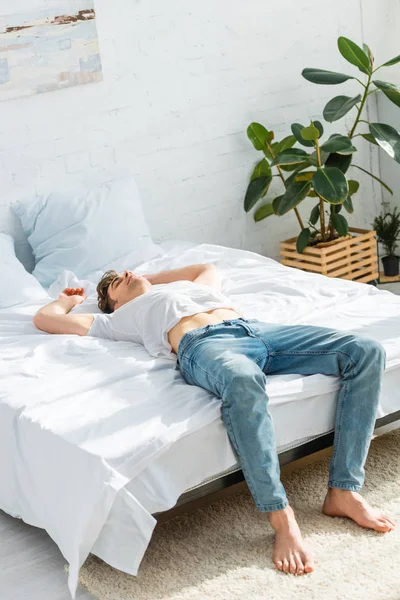 Mann in T-Shirt und Jeans liegt auf Rücken auf Bett im Schlafzimmer — Stockfoto