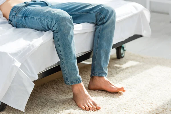 Vista cortada do homem em jeans deitado na cama no quarto — Fotografia de Stock