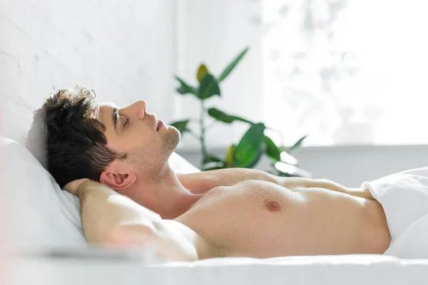 Handsome man sleeping on bed with bare torso near window in bedroom — Stock Photo