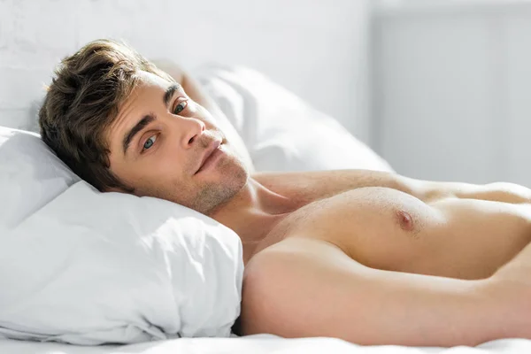 Handsome man lying on bed and pillow with bare torso in bedroom — Stock Photo