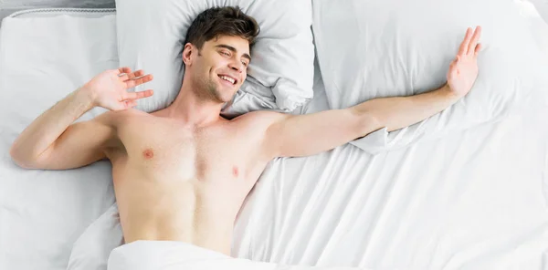 Panoramic shot of man with bare torso stretching in bad at home — Stock Photo