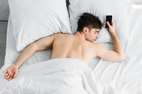 Handsome man sleeping under blanket near smartphone with blank screen on bad — Stock Photo
