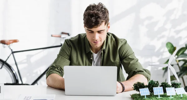 Bello architetto in camicia verde seduto a tavola con computer portatile in ufficio — Foto stock