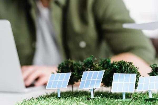 Foco seletivo de painéis solares e modelos de árvores na mesa perto do arquiteto no escritório — Fotografia de Stock