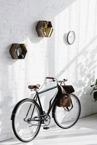 Bicicleta negra con bolsa cerca de la pared de ladrillo blanco en la oficina - foto de stock