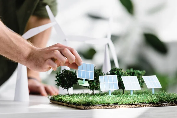 Vista recortada del hombre poniendo paneles solares modelos sobre hierba en la mesa en la oficina - foto de stock