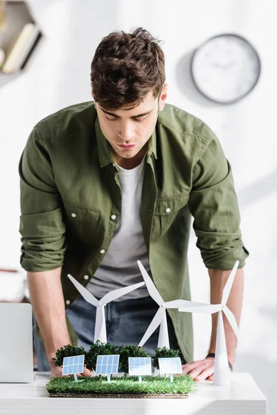 Handsome architect standing over table with trees, windmills, solar panels models on grass in office — Stock Photo