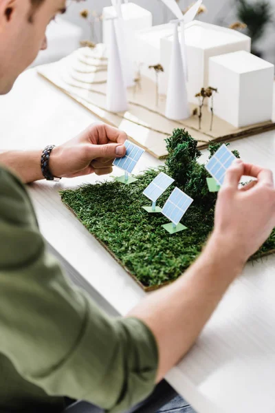 Vista recortada del arquitecto sosteniendo modelos de paneles solares sobre mesa en la oficina — Stock Photo