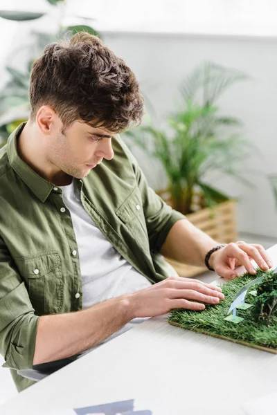 Selective focus of handsome architect sitting at table with solar panels models on grass in office — Stock Photo
