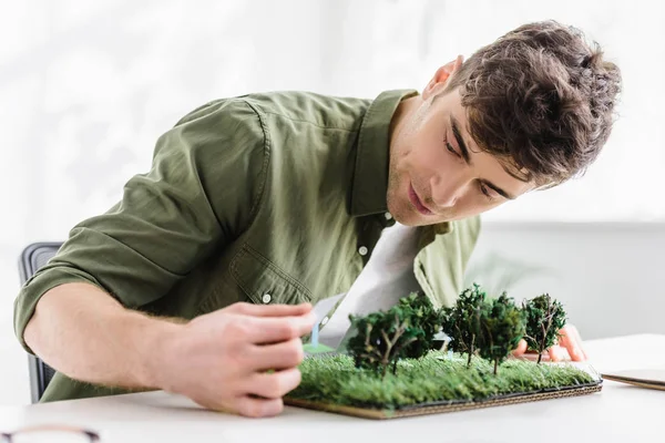 Beau architecte assis à la table et de mettre des modèles de panneaux solaires sur l'herbe dans le bureau — Photo de stock