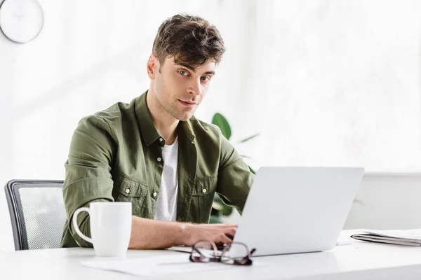 Man in green shirt sitting at table with laptop and typing in office — Stock Photo