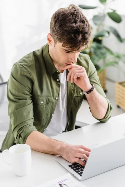 Bell'uomo d'affari in camicia verde seduto a tavola con computer portatile e digitando in ufficio — Foto stock