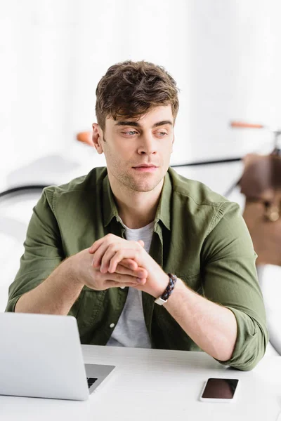 Homme d'affaires en chemise verte assis à table avec ordinateur portable et smartphone et dactylographier dans le bureau — Photo de stock