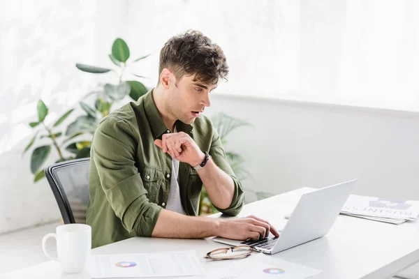 Handsome businessman in shirt sitting at table with laptop and typing in office — Stock Photo